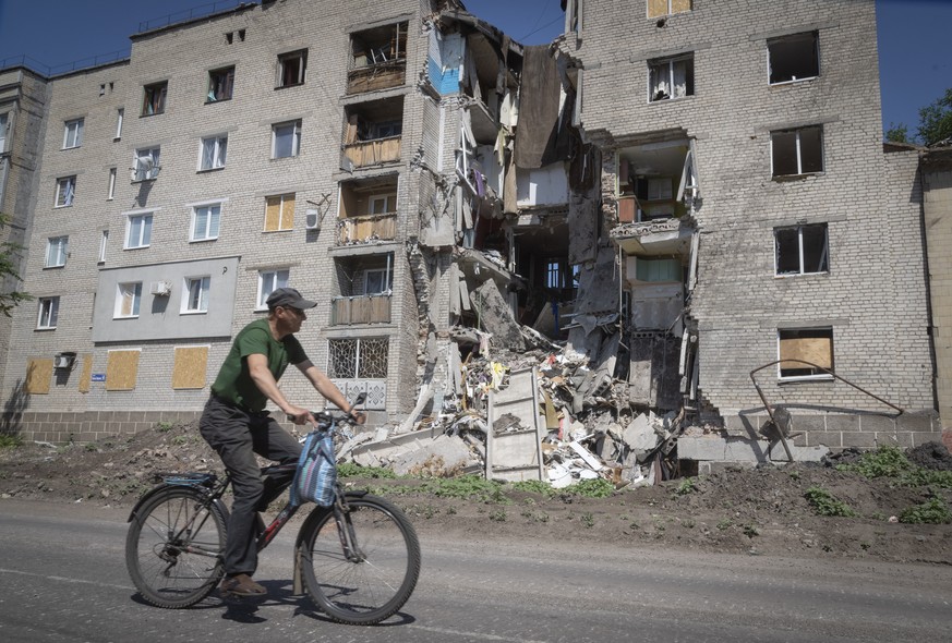 A man rides a bicycle past a building damaged in Russian shelling in Bakhmut, Donetsk region, Ukraine, Monday, June 20, 2022. (AP Photo/Efrem Lukatsky)