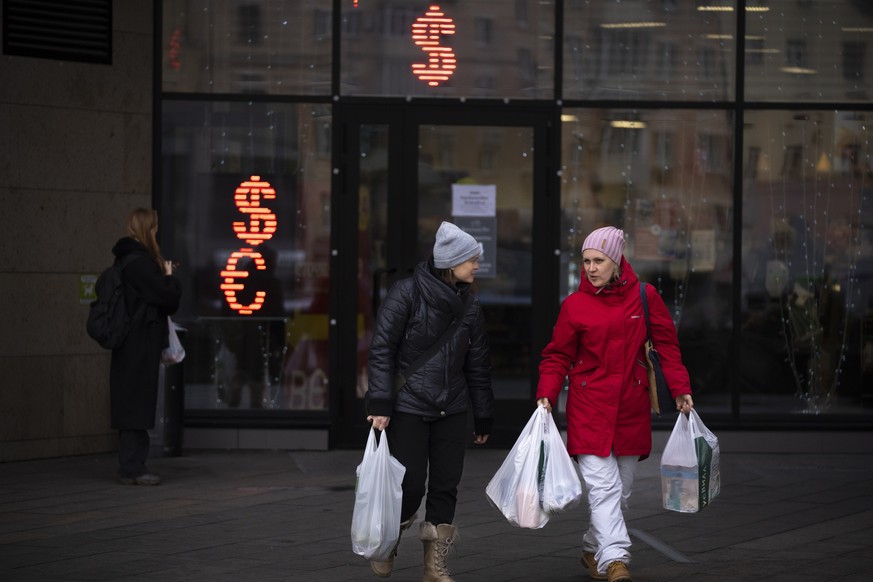 Two women walk past a currency exchange office screen displaying the exchange rates of U.S. Dollar and Euro to Russian Rubles in Moscow, Russia, Friday, April 1, 2022.