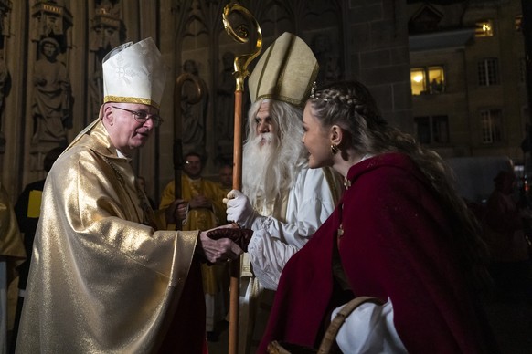 A man disguised as St. Nicolas, center, welcomes Charles Morerod roman Catholic Bishop of Lausanne, Geneva and Fribourg, left, after the procession for the Saint Nicolas prior to delivering his speech ...