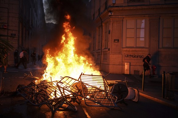 A man passes by a wall illuminated by a burning barricade on which is written 'Police kills' in the center of Lyon, central France, Friday, June 30, 2023. French President Emmanuel Macron ur ...