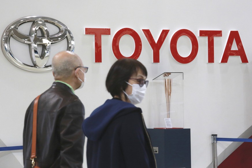 FILE - People walk past the logo of Toyota at a showroom in Tokyo, Monday, Oct. 18, 2021. Toyota is suspending production at all 28 lines of its 14 plants in Japan starting Tuesday, because of a