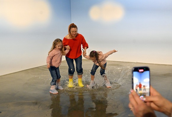 A family jumps in an artificial puddle during a visit at the &quot;Third Wind. Emotions and Feelings&quot; interactive exhibition in Kyiv, on April 27, 2025. The exhibition, at the discretion of the o ...