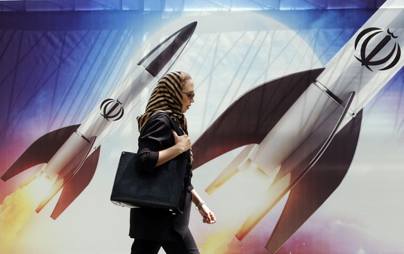 epa11281648 An Iranian woman walks past an anti-Israel banner carrying pictures of Iranian missiles, in Tehran, Iran, 16 April 2024. Iranian President Ebrahim Raisi on 14 April said any new targeting  ...