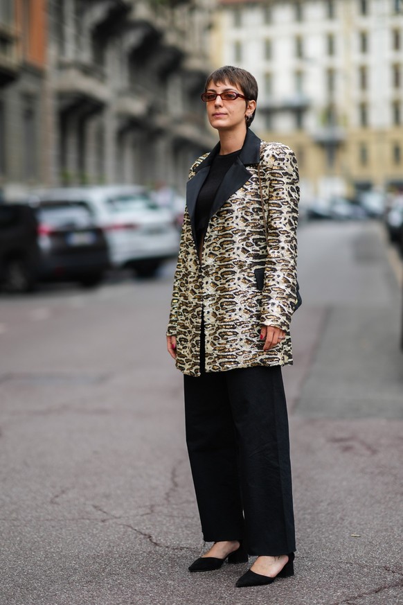 MILAN, ITALY - SEPTEMBER 25: A guest wears red sunglasses, a black t-shirt, a white / black / brown leopard sequined embroidered pattern long blazer jacket, black large pants, black suede pointed bloc ...