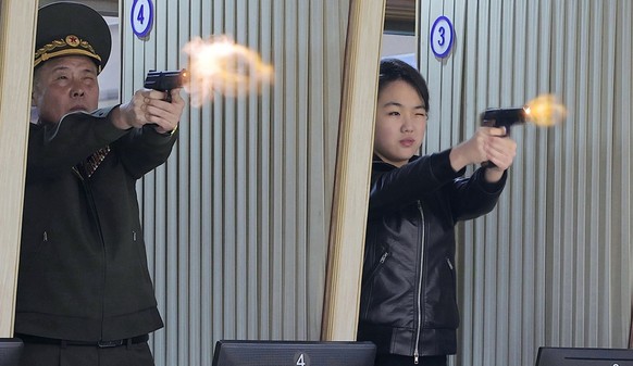 In this photo provided by the North Korean government, its leader Kim Jong Un's daughter, center, tries out a new pistol at a factory producing pistols and other light arms at an undisclosed plac ...