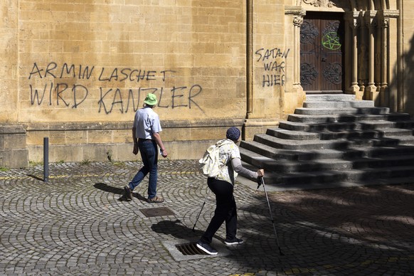 Besucher schauen auf Sprayereien an einer Wand der Kollegiatkirche Neuenburg (Collegiale de Neuchatel) an, am Dienstag, 5. August 2025 in Neuchatel. (KEYSTONE/Peter Klaunzer)