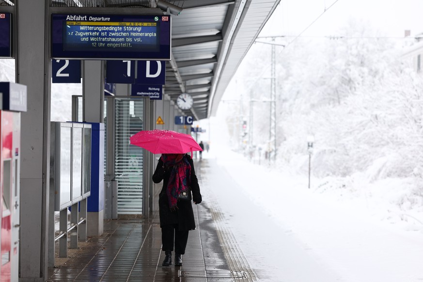 epa11007146 A woman walks along a train platform amid heavy snow in Munich, Germany, 02 December 2023. Due to heavy snowfall, flight operations at Munich Airport have been temporarily suspended until  ...