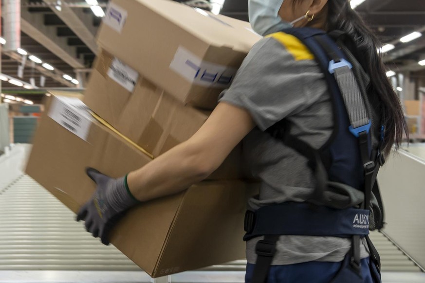Eine Angestellte traegt ein Exoskelett bei der Sortierung der Pakete im regionalen Paketzentrum der Post in Basel, am Donnerstag, 25. November 2021. (KEYSTONE/Georgios Kefalas)