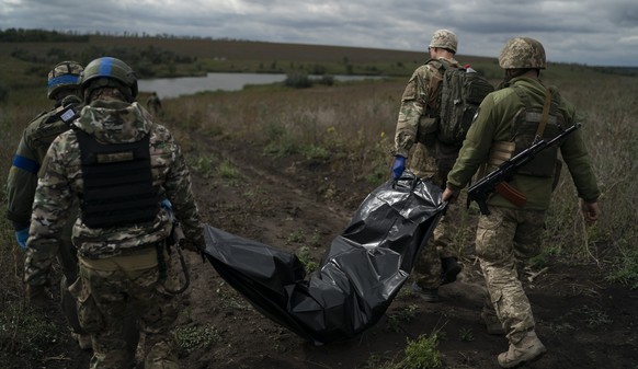 Ukrainian national guard servicemen carry a bag containing the body of a Ukrainian soldier in an area near the border with Russia, in Kharkiv region, Ukraine, Monday, Sept. 19, 2022. This region of ro ...
