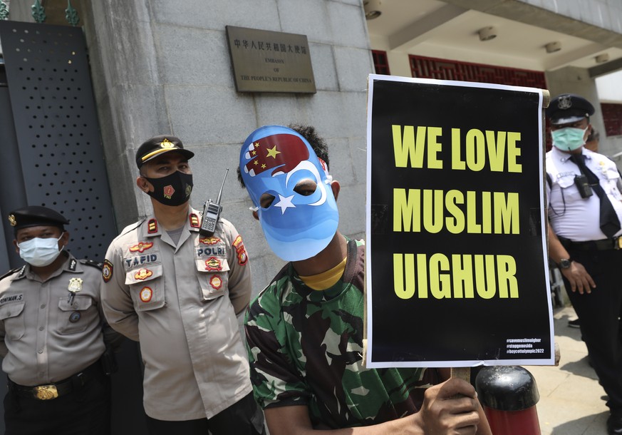 FILE - In this March 25, 2021, file photo, a Muslim student wearing a mask with the colors of the pro-independence East Turkistan flag, and the Chinese national flag in the shape of a hand holds a pos ...