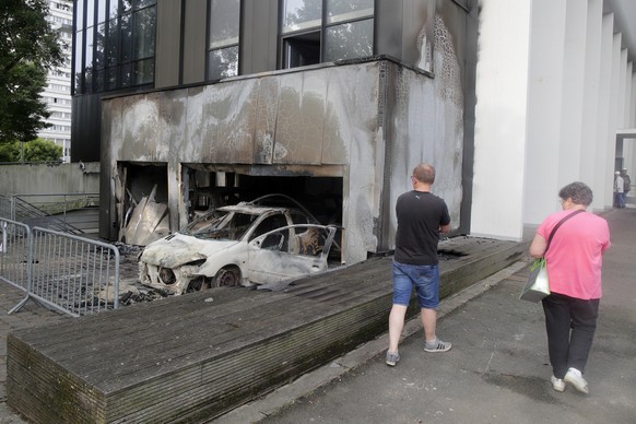 Residents walk past a charred car at the town hall of Mons-en-Bar?ul, northern France Thursday, June 29, 2023. Protesters angry after police shot a 17-year-old boy dead set cars and buildings ablaze i ...