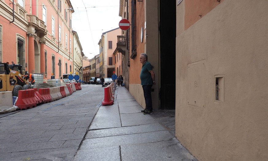 BOLOGNA, ITALY - CIRCA SEPTEMBER 2022: Umarell man of retirement age watching roadworks construction site with hands clasped behind his back and offering unwanted advice to the workers