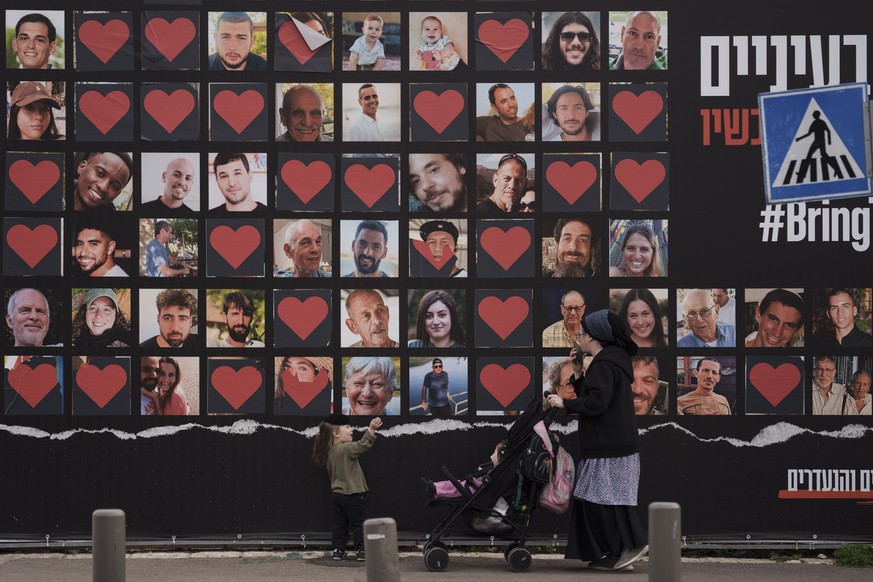 FILE - A woman and her children walk past a wall with photographs of hostages who were kidnapped during the Oct. 7, 2023, Hamas cross-border attack in Israel, Feb. 26, 2024, in Jerusalem. On Monday, J ...