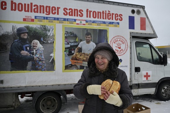 A woman reacts as she holds loaves of freshly baked bread distributed by French volunteer baker Loic Nervi from his mobile bakery among residents of a temporary dwelling for people who lost their home ...