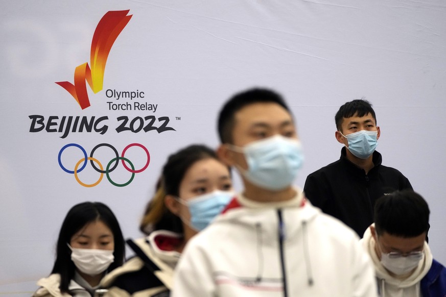 Participants wearing face masks sit near a logo for the Olympic torch relay for the 2022 Winter Olympics during an event at the Beijing University of Posts and Communications in Beijing, Thursday, Dec ...