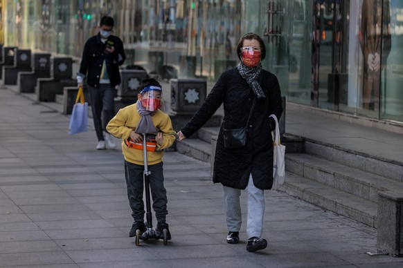 epa09843714 A woman and child wearing protective gear walk on the street in Shanghai, China, 23 March 2022. According to the National Health Commission, more than 2,500 new Covid-19 cases were detected in China on 23 March. Authorities in Shanghai denied rumors of a citywide lockdown that led to panic-buying. Online grocery stores ran out of stock on 22 March and no delivery men were available.  EPA/ALEX PLAVEVSKI