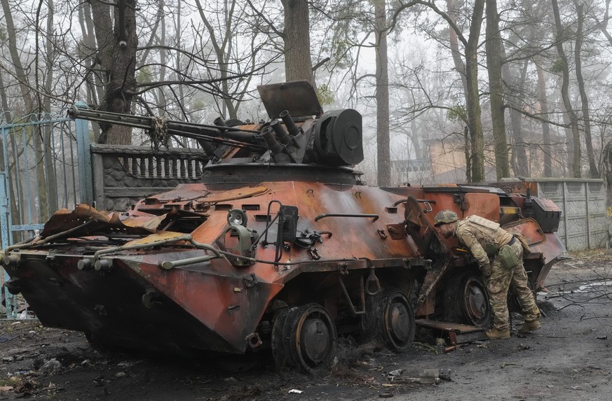 A Ukrainian soldier examines a destroyed military vehicle after recent battles in Irpin close to Kyiv, Ukraine, Friday, April 1, 2022. The more than month-old war has killed thousands and driven more  ...