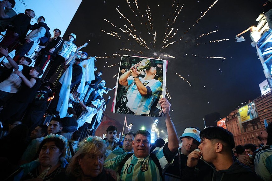 BUENOS AIRES, ARGENTINA - JULY 15: A fan of Argentina raises an image of Diego Maradona as fireworks light in the background during the celebrations after their team's victory in the FIFA World C ...