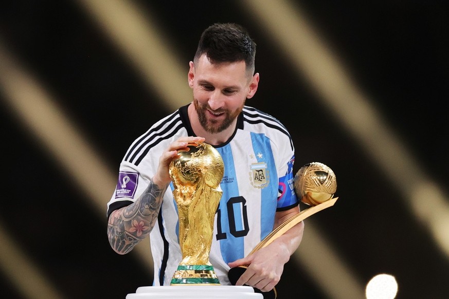epa10373265 Lionel Messi of Argentina touches the World Cup trophy as he passes it after winning the golden ball award during the awards ceremony after the FIFA World Cup 2022 Final between Argentina  ...