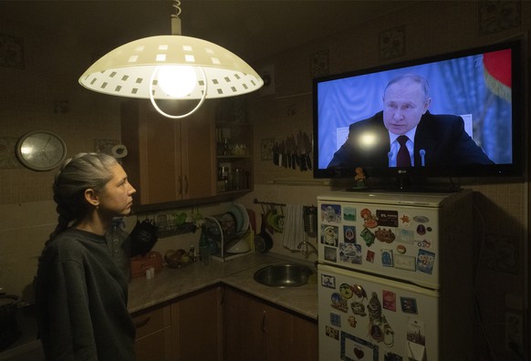 epaselect epa09775854 A woman watches TV with Russian President Putin speaking during a broadcast of a meeting of the National Security Council on the recognition of the self-proclaimed Donetsk People ...