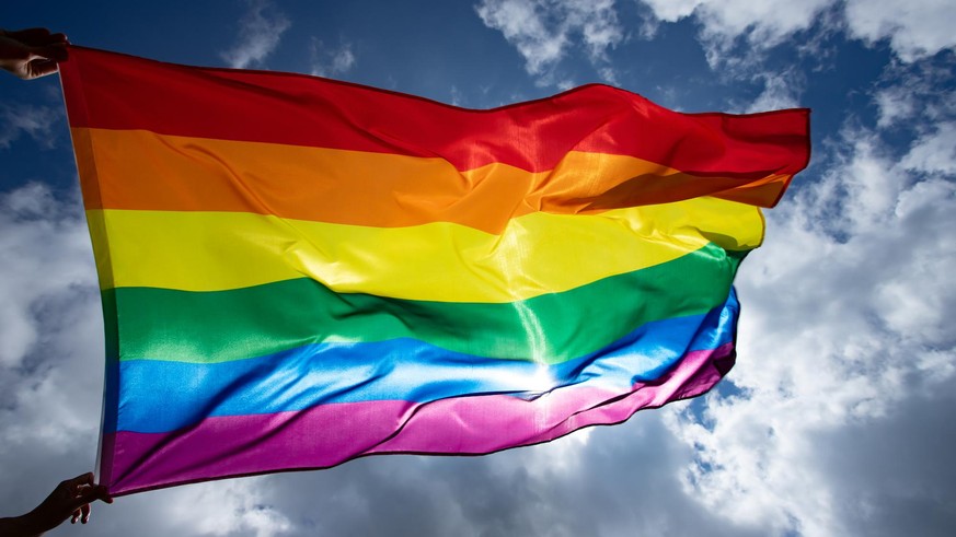 Bright rainbow LGBT flag fluttering against blue sky.