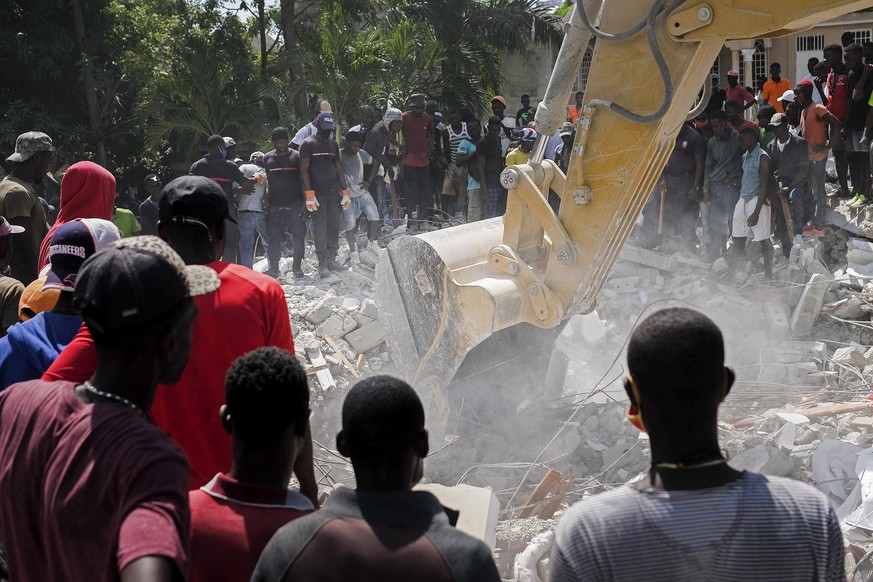 People watch a bulldozer remove debris at the collapsed Le Manguier hotel in Les Cayes, Haiti, Monday, Aug. 16, 2021, two days after a 7.2-magnitude earthquake struck the southwestern part of the coun ...