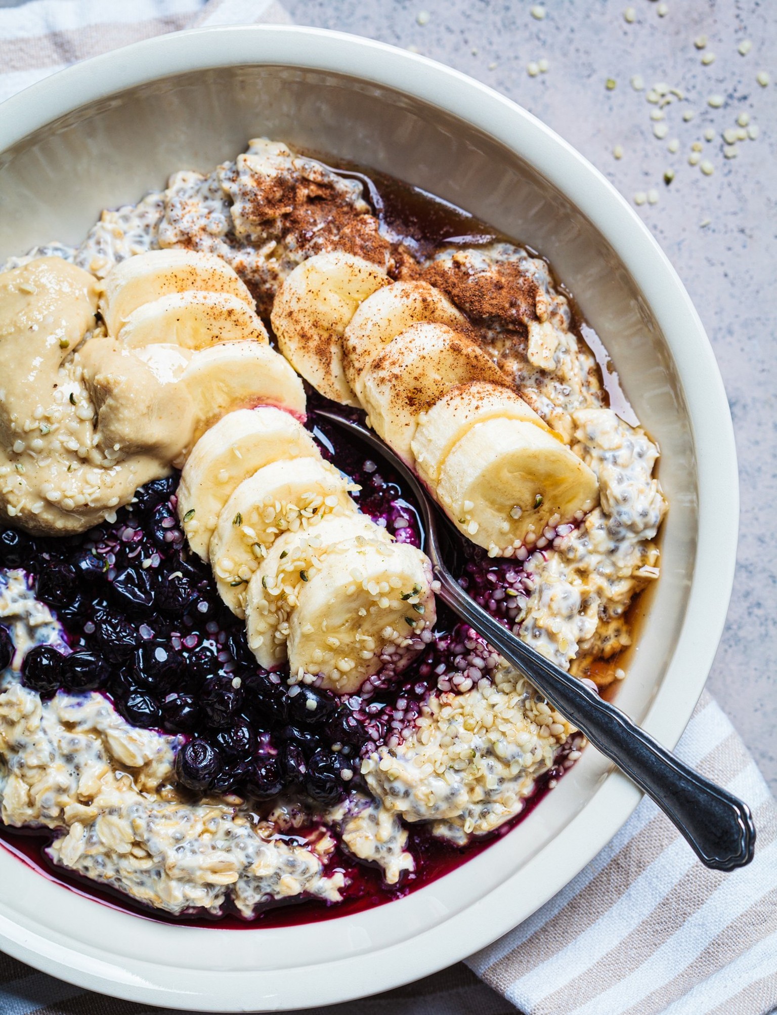 Winter breakfast concept. Overnight oatmeal with banana, berry, chia seeds, sesame tahini, cinnamon and syrup in bowl, top view, dark background.