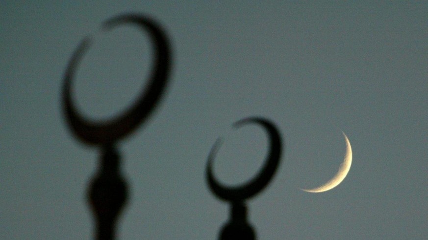 The moon seen behind the silloutte of the crescents on top of the dome of the Cultural Square Mosque, on the second evening of Ramadan, the Muslim holy month of fasting, in Sharjah, United Arab Emirat ...