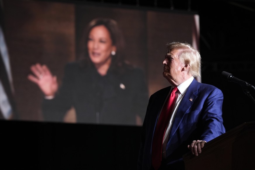 Republican presidential nominee former President Donald Trump speaks as an image of democratic presidential candidate Vice President Kamala Harris appears on screen during a campaign event at the Worl ...