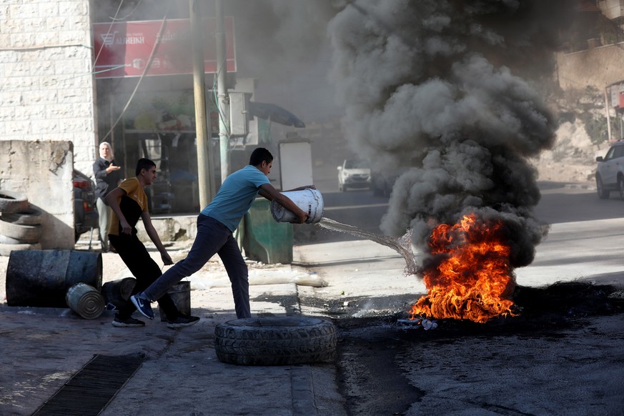 epa09489581 A man throws water at burning tires before the funeral of late 22-year-old Osama Sobh, killed in an Israeli overnight military raid, at Burqin village, near the West Bank city of Jenin, 26 ...