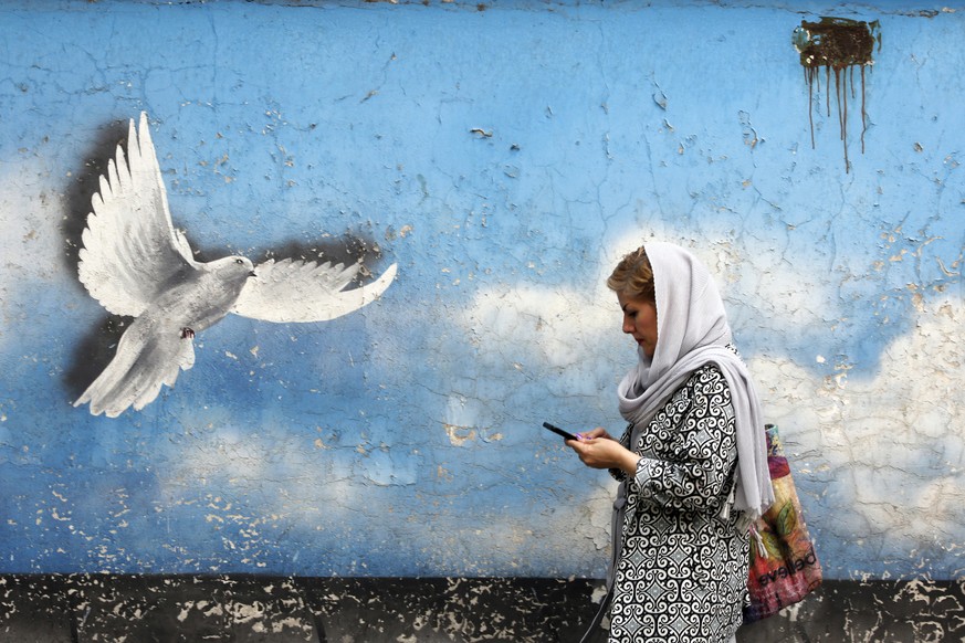 epa10101278 An Iranian woman walks past a wall painting of peace bird in a street in downtown of Tehran, Iran, 01 August 2022. According to Iranian foreign ministry there will likely be a new round of ...