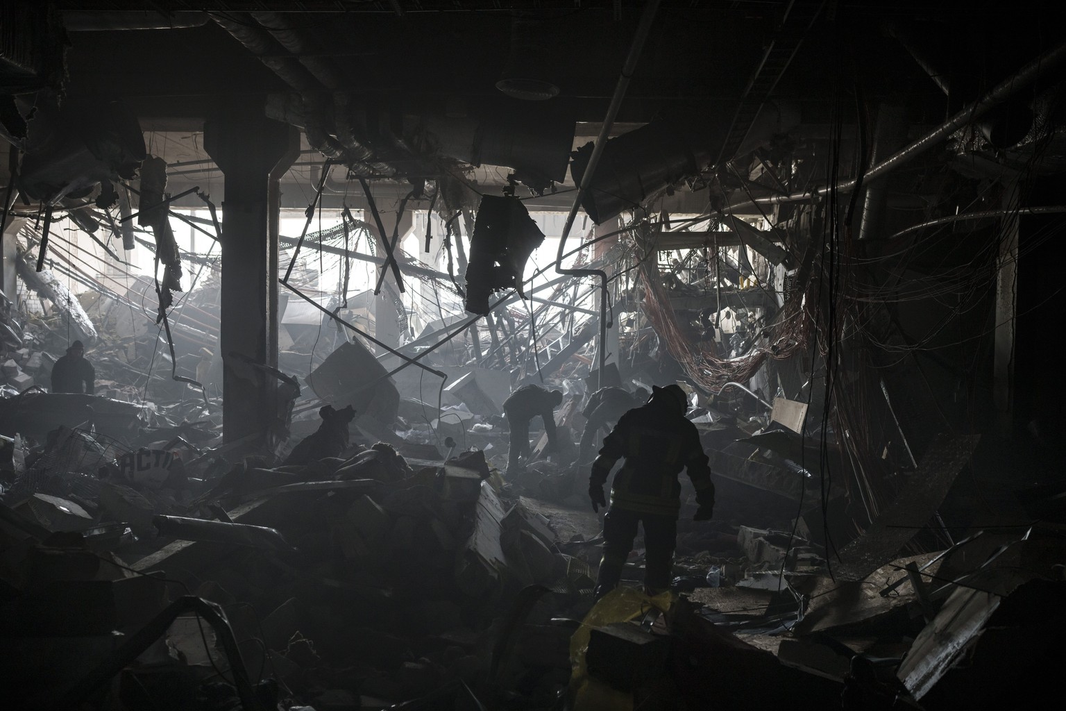 Ukrainian firefighters and servicemen search for people under debris inside a shopping center after bombing in Kyiv, Ukraine, Monday, March 21, 2022. (AP Photo/Felipe Dana)