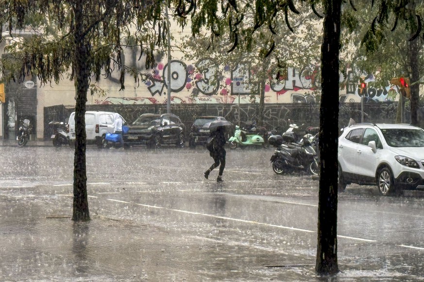 epa11692534 A person crosses a street under a heavy rain in Barcelona city, Catalonia, north-eastern Spain, 30 October 2024. An alert on rough weather in Barcelona province has being launched by Catal ...