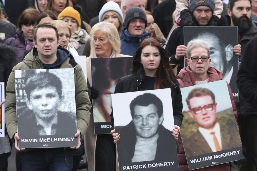 Des personnes tiennent des photos de certaines des victimes à Londonderry lors d'une marche de commémoration, dimanche 30 janvier 2022.