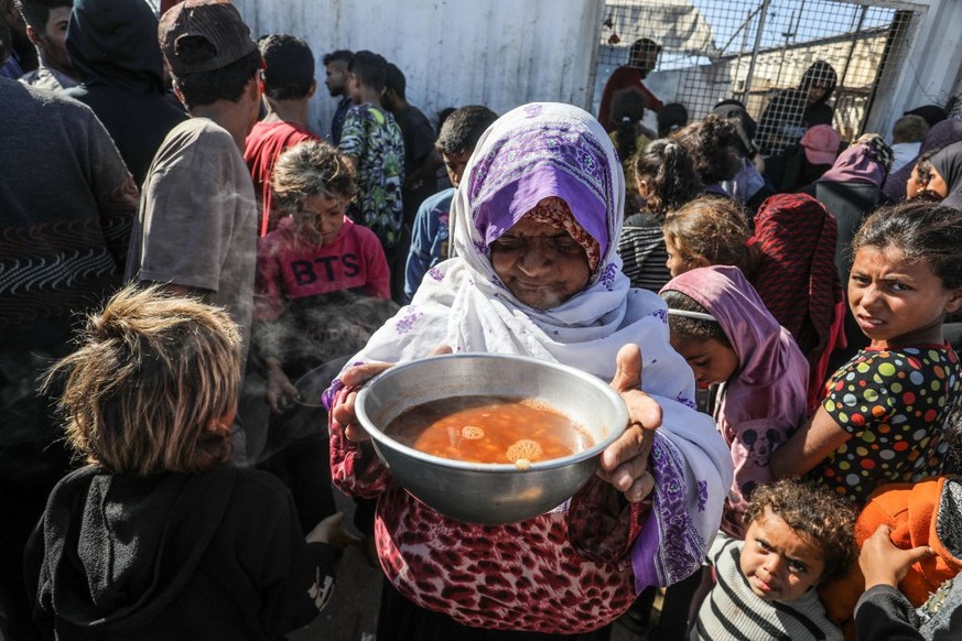 KHAN YUNIS, GAZA - NOVEMBER 16: A woman who can take the food distributed carries her food as Palestinians, including children, who escaped from the attacks of the Israeli army and took shelter in the ...