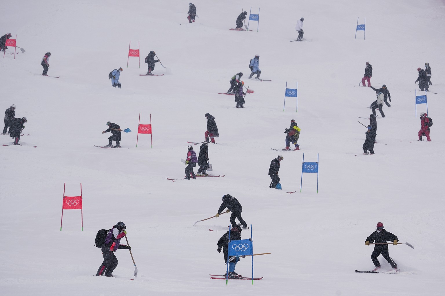 Workers clear snow from the course after the second run of the men&#039;s giant slalom was delayed due to a heavy snowfall at the 2022 Winter Olympics, Sunday, Feb. 13, 2022, in the Yanqing district o ...