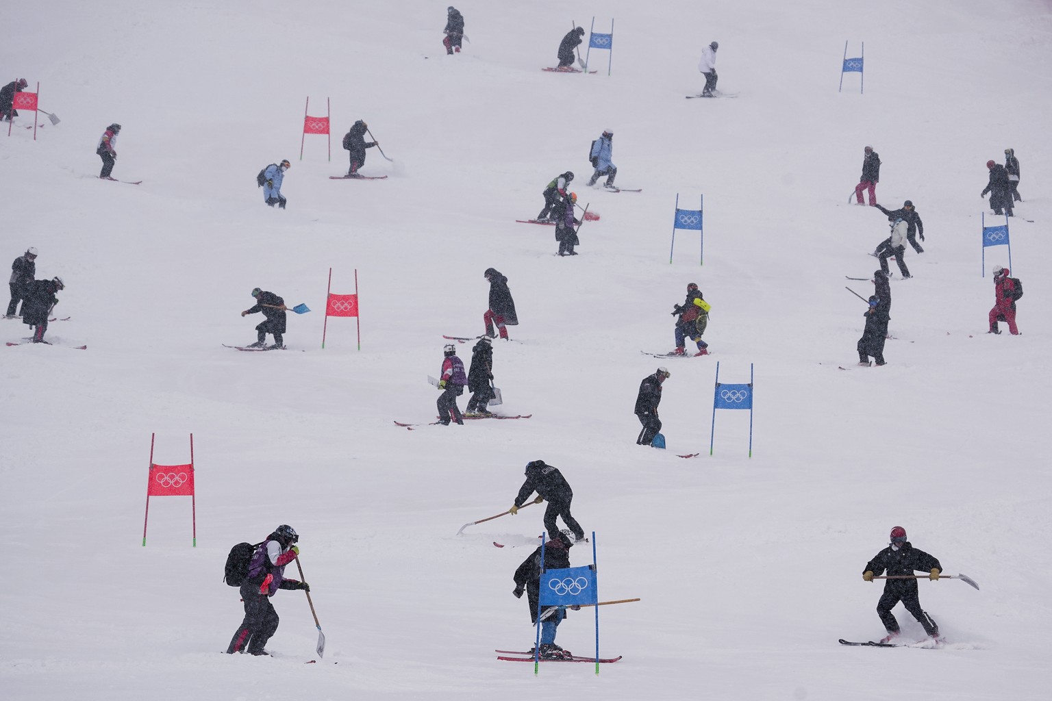 Workers clear snow from the course after the second run of the men's giant slalom was delayed due to a heavy snowfall at the 2022 Winter Olympics, Sunday, Feb. 13, 2022, in the Yanqing district o ...