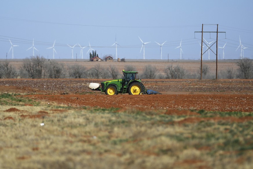 A farmer uses a tractor to plow a cotton field as wind turbines give backdrop Wednesday, Feb. 26, 2025, in Lamesa, Texas. (AP Photo/Julio Cortez)