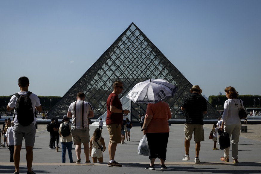 A tourist holds an umbrella in the courtyard of the Louvre museum, Thursday, Sept. 7, 2023 in Paris where temperatures rose up to 33 degrees Celsius (91 degrees Fahrenheit ). (AP Photo/Thomas Padilla)