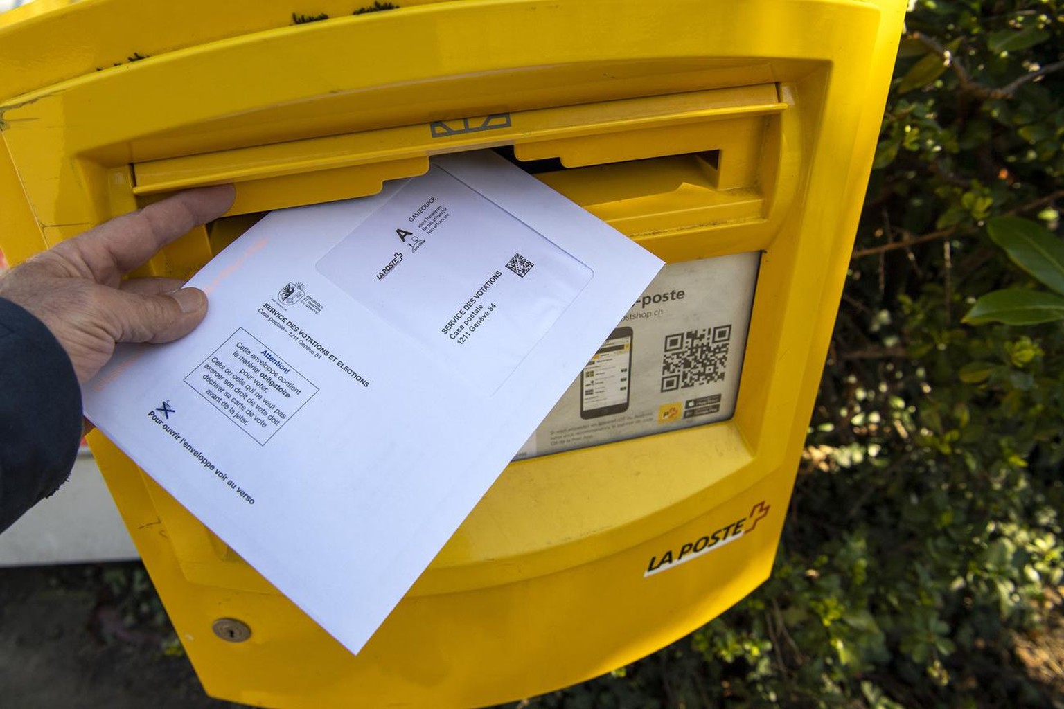 Une personne met son enveloppe de vote dans une boite aux lettres de la poste pour le service des votations, qui contient son materiel de vote et les bulletins pour le second tour de l&#039;election c ...