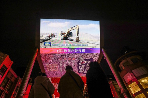epa11810952 People watch a screen broadcasting the evening news about the 6.8-magnitude earthquake that struck Tibet, in Beijing, China, 07 January 2025. At least 95 people have been confirmed dead an ...