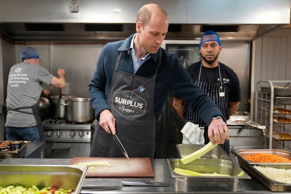 SUNBURY, ENGLAND - APRIL 18: Prince William, Prince of Wales speaks with head chef Mario Confait, (R) as he cuts celery while helping to make a bolognese sauce during a visit to Surplus to Supper, in  ...
