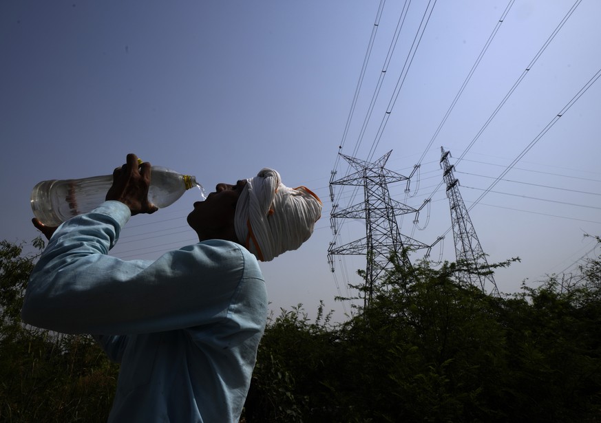 A workers quenches his thirst next to power lines as a heatwave continues to lashes the capital, in New Delhi, India, Monday, May 2, 2022. An unusually early and brutal heat wave is scorching parts of ...