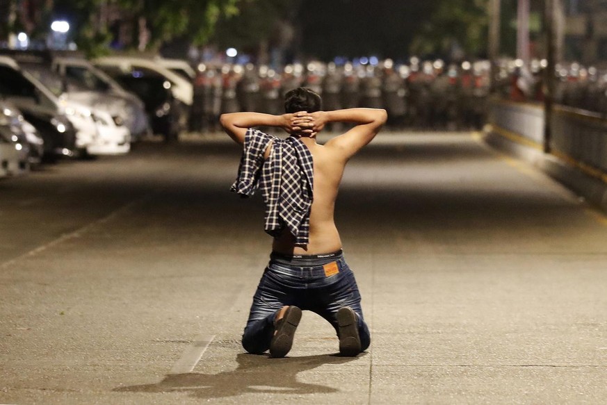 epa09035621 A demonstrator kneels as he protests against the military coup while riot police advance on a street as tensions rise in Yangon, Myanmar, 25 February 2021. Anti-coup demonstrations continu ...
