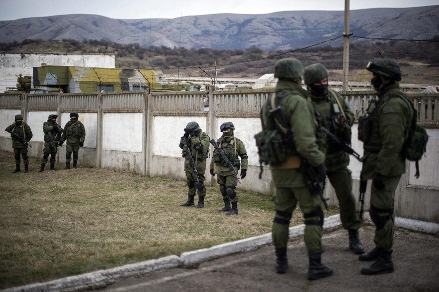 epa04106438 Armed men in military uniform walk outside the territory of a Ukrainian military unit in the village of Perevalnoye, outside Simferopol, Ukraine, 2 March 2014. Russia ratcheted tension in  ...