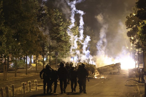 Riot police officers patrol as smoke billows from burnt vehicles on the third night of protests sparked by the fatal police shooting of a 17-year-old driver in the Paris suburb of Nanterre, France, Fr ...