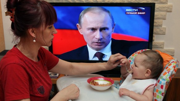 epa01953485 A woman spoon-feed a baby as the television displays Russian Premier Vladimir Putin during live call-in show, in Moscow, Russia, 03 December 2009. State news channels broadcasted the show. ...