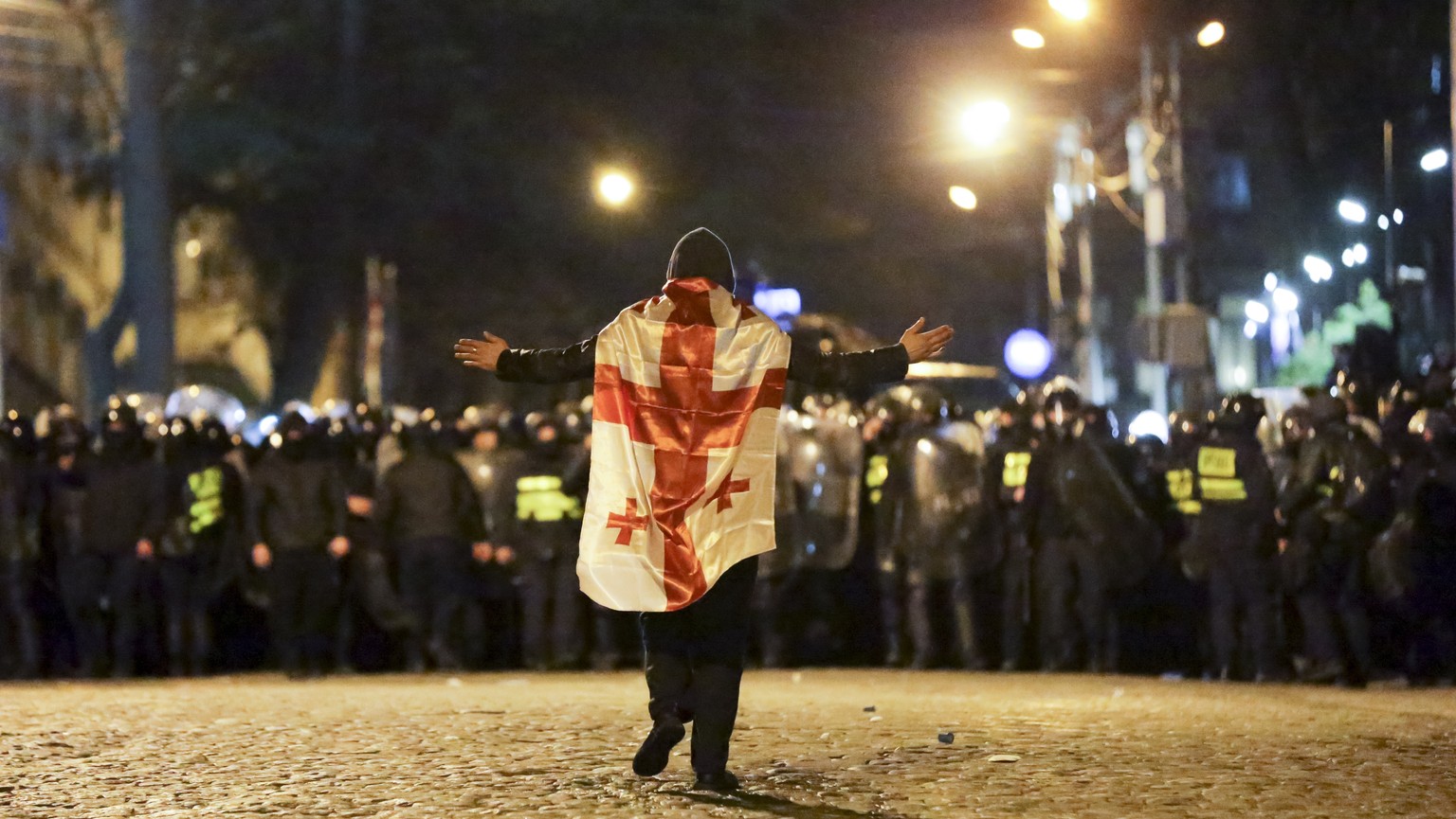 A protester wearing a Georgian national flag walks toward police line outside the Georgian parliament building in Tbilisi, Georgia, Tuesday, March 7, 2023. Georgian authorities used tear gas and water ...