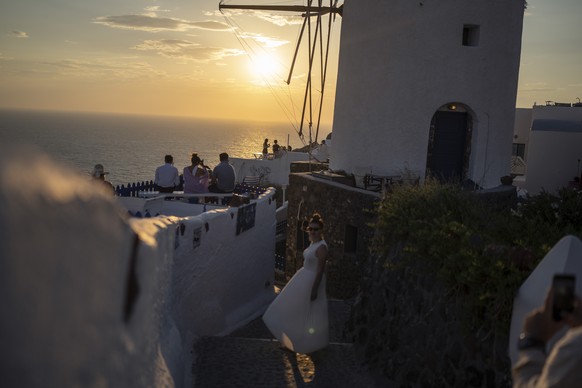 A woman poses for a picture as other tourists look on as the sun sets in the Aegean Sea, Oia, Santorini island, Greece, on Monday, June 13, 2022. (AP Photo/Petros Giannakouris)