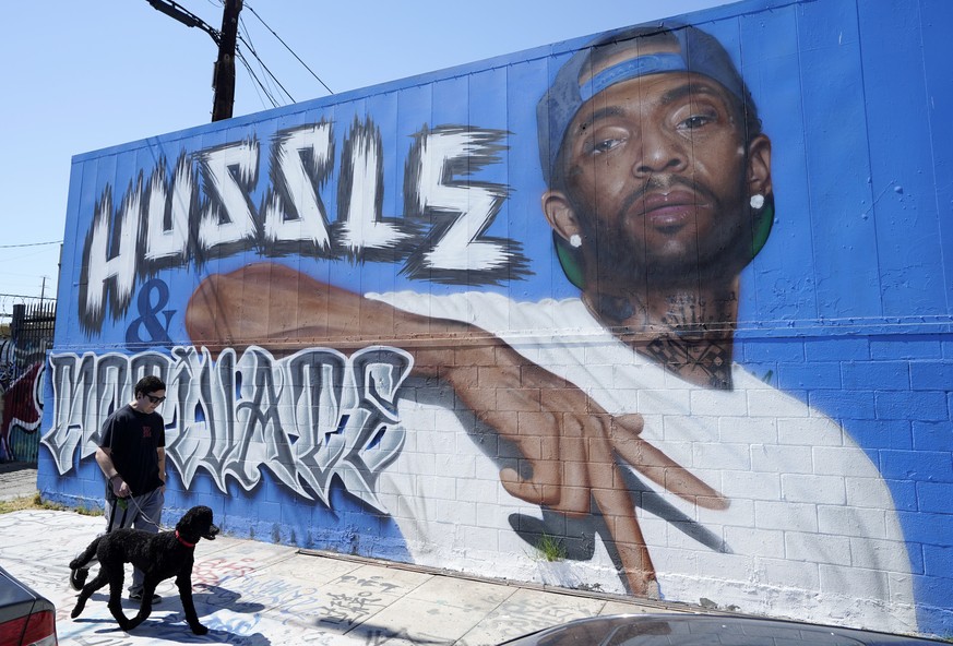 A man walks his dog past a street mural of the late rapper Nipsey Hussle, Tuesday, June 28, 2022, in downtown Los Angeles. The many murals of Hussle around Los Angeles speak to the late rapper&#039;s  ...